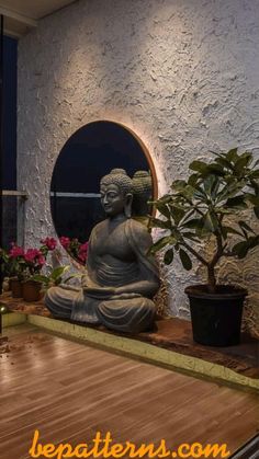 a buddha statue sitting on top of a wooden floor next to a potted plant