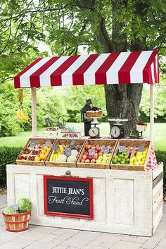 an outdoor fruit stand with red and white striped awning on the side of it