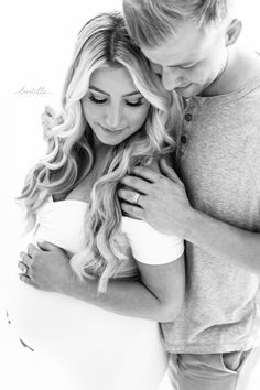 a pregnant couple cuddles in black and white for their newborn photo session at the studio