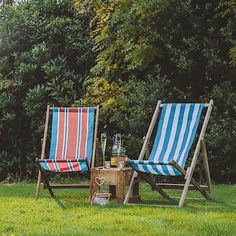 two lawn chairs sitting next to each other on top of a lush green field with trees in the background