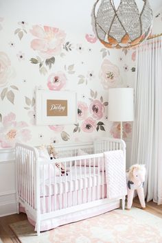 a baby's room decorated in pink, white and gold with floral wallpaper