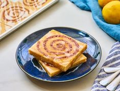 two slices of cinnamon roll on a blue plate next to lemons and utensils