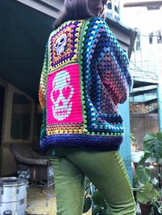 a woman in green pants is wearing a colorful crocheted jacket with skulls on it