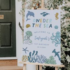 a welcome sign with sea animals on it in front of a door and green plants