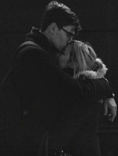 a black and white photo of a man kissing a woman's face with his arms around her