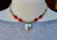 Beautiful Christmas beaded czech glass necklace with a silver heart pendant and holly on it.  A pretty necklace for the upcoming holiday season.  There are red czech glass Christmas trees on it, a few miyuki seed beads in 11/0, czech glass green sparkly crystal bicones and a silver lobster clasp.  It is 15 inches long.  If you need an extender chain just message me.  Everything is nickel free.  I usually ship in a brown jewelry box so if you want a Christmas box just let me know. Everything in my store is nickel free.  If you have any questions just message me. This heart necklace makes perfect Christmas gifts for her. To visit my Etsy store click here: https://www.etsy.com/shop/BNJewelryAndArtwork Here Are A Few Details about my handmade jewelry: * I use very strong bead stringing wire fo Green Heart-shaped Beaded Necklace Gift, Heart Beads Pendant Necklace For Gifts, Gift Czech Glass Heart Beaded Necklaces, Heart Charm Beaded Pendant Necklace For Gift, Handmade Heart Pendant Beaded Necklace As Gift, Silver Beaded Necklace For Valentine's Day Gift, Silver Heart-shaped Beaded Necklace For Gift, Green Holiday Jewelry Gift, Holiday Gift Green Jewelry