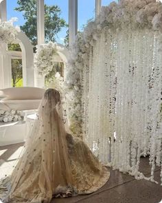 a woman in a wedding dress standing next to a white arch with flowers on it