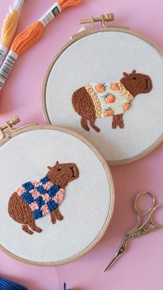 two embroidered bears sitting next to each other on top of a pink surface with scissors and thread