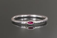 a silver ring with a red stone on it's side, sitting on a table