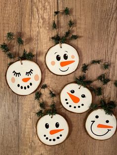 four snowmen painted on wood slices hanging from a string with pine branches around them