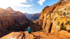 a person sitting on the edge of a cliff looking down at mountains and canyons