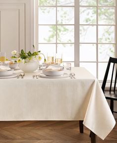 the table is set for two with white dishes and glasses on it, along with yellow flowers