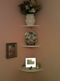 three white shelves with flowers and plates on them in a bathroom wall mounted above a toilet