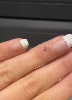 a woman's hand with white nail polish and a heart tattoo on her finger