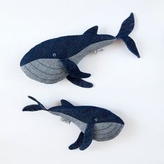 two stuffed whales sitting next to each other on a white surface with blue and gray colors