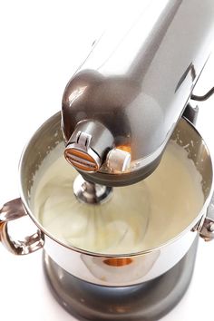 an electric mixer is being used to make cream in a saucepan on a white background