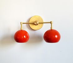 two red balls are hanging from a gold wall mounted light fixture on a white wall