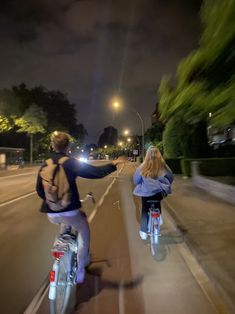 two people riding bikes down the street at night with their arms out to each other