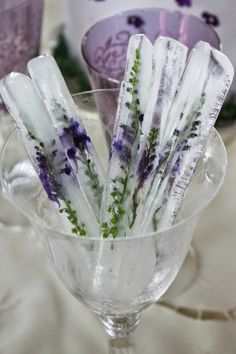 purple and white flowers are placed in an ice - filled martini glass on a table