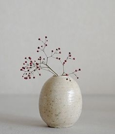 a white vase with some red flowers in it on a gray tableclothed surface