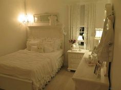 a white bedroom with a bed, dresser and mirror in it's corner next to a window