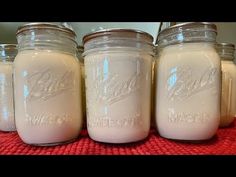 four jars filled with white liquid sitting on top of a red table cloth next to each other