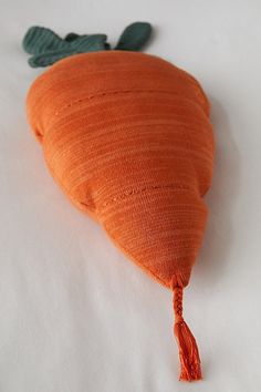 an orange carrot shaped pillow with tassels on it's sides, laying on a white surface