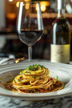 a white plate topped with spaghetti next to a glass of wine