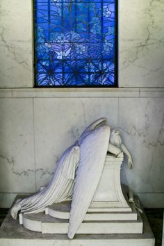 an angel statue in front of a blue stained glass window at the end of a stairway