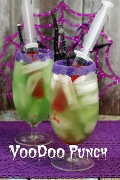 two glasses filled with liquid sitting on top of a purple tablecloth next to a wooden fence