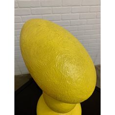 a large yellow sculpture sitting on top of a black table next to a white brick wall