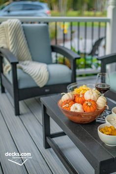 a wooden table topped with bowls filled with pumpkins and gourmet food next to two chairs