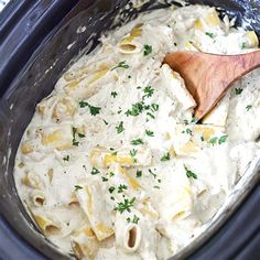 a wooden spoon in a slow cooker filled with pasta and sauce, garnished with parsley