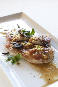 a white plate topped with meat covered in sauce and garnished with parsley