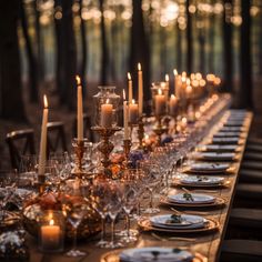 a long table is set with candles and place settings for an outdoor dinner in the woods