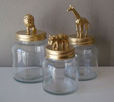 three glass jars with gold figurines sitting on top of each other in front of a white wall