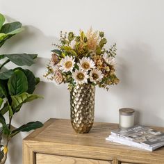 a vase filled with lots of flowers sitting on top of a wooden table next to a potted plant