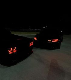 two black sports cars are parked in the parking lot at night with their lights on