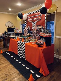 an orange table with black and white checkered cloths, balloons, and streamers