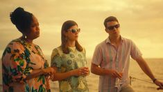 three people standing on the deck of a boat near the ocean at sunset or sunrise