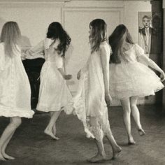 four women in white dresses are walking around the room with their feet on the floor