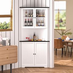 a white cabinet filled with lots of bottles and glasses next to a dining room table