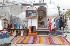 an outdoor market with luggage and rugs on the ground, including clothes hanging up