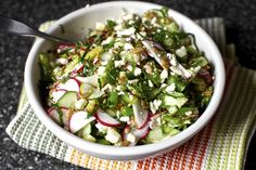 a white bowl filled with cucumber and radishes on top of a table