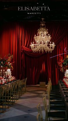 an event venue with red curtains and chandelier in the center is set up for a formal function