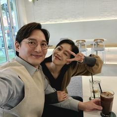 a man and woman posing for a photo in front of a coffee shop with their fingers up