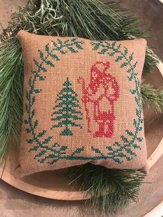 a small pillow on top of a wooden plate next to evergreen branches and pine cones