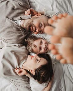 two people laying in bed with their arms around each other and looking at the camera