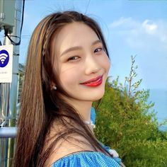 a woman with long brown hair and red lipstick smiles at the camera while standing in front of a gas station sign