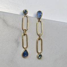 a pair of earrings with blue stones hanging from it's sides on a marble surface